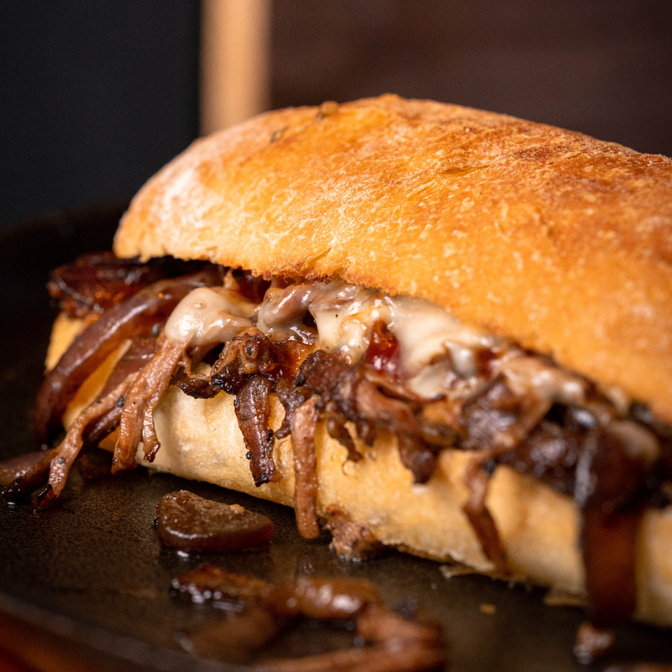 Close-up of a Philly cheesesteak sandwich with melted cheese and caramelized onions on a dark surface.