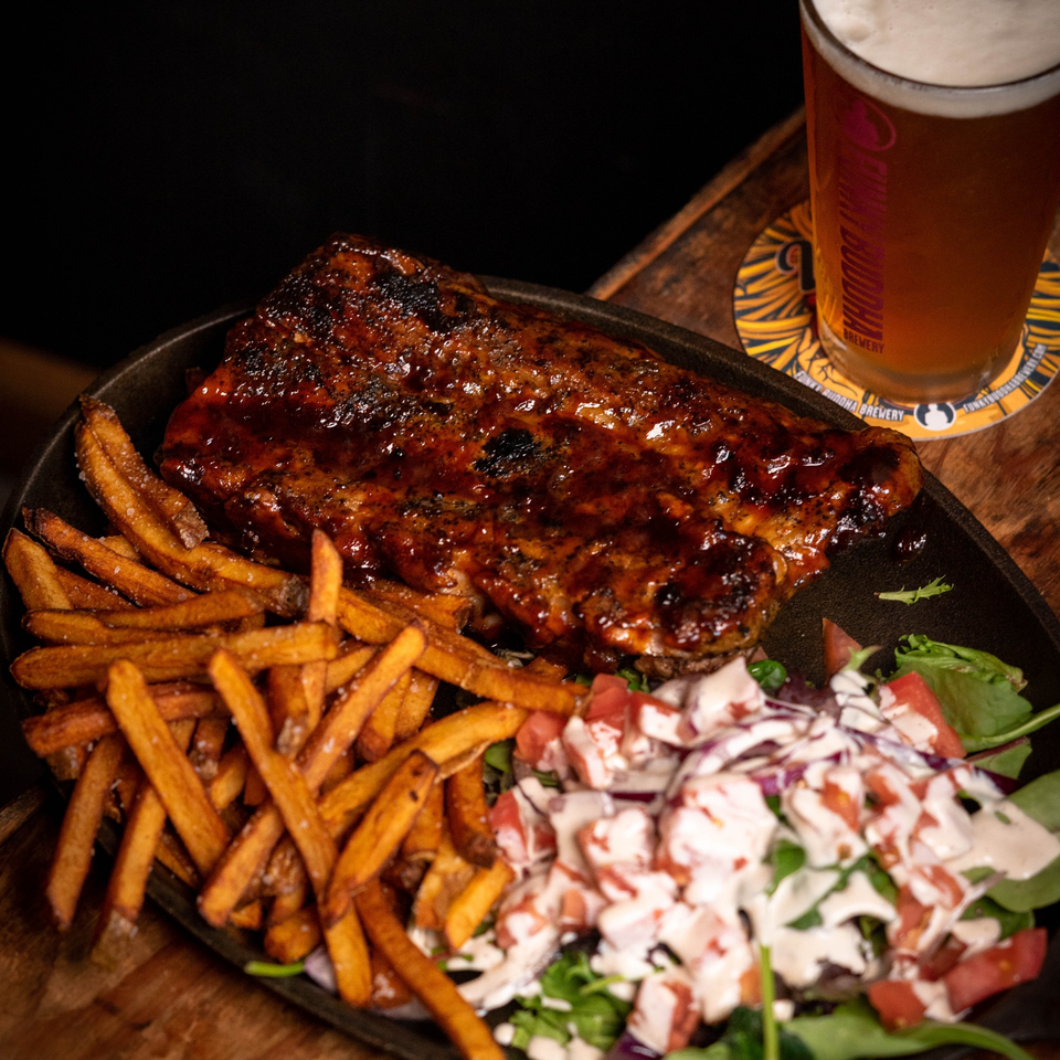 Ribs with BBQ sauce, sweet potato fries, and a side salad with dressing, next to a beer.