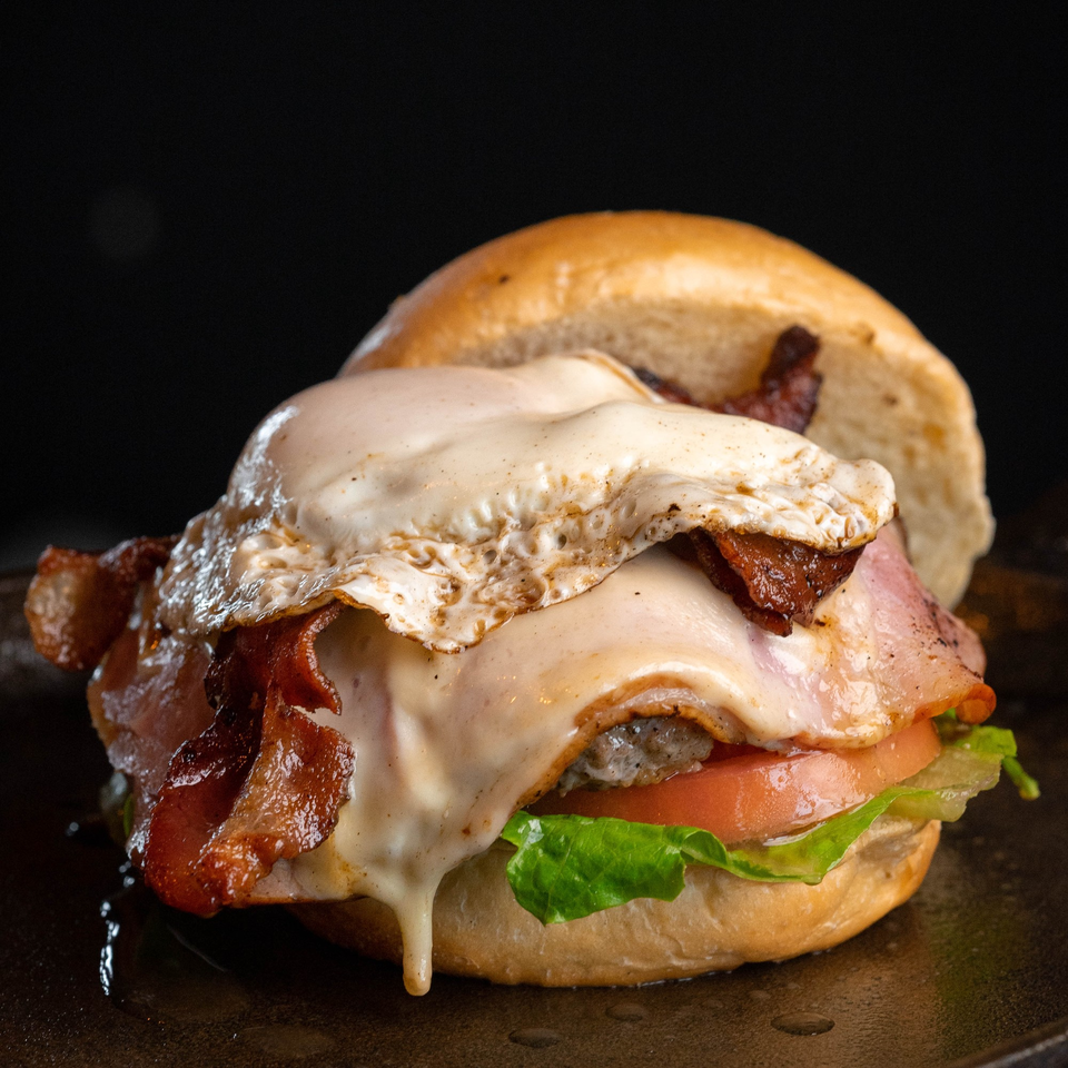 A Blues Burgers burger with a fried egg, bacon, melted cheese, lettuce, and tomato.
